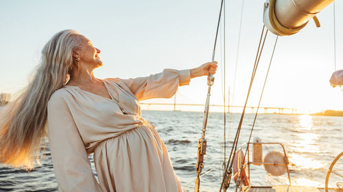 Senior woman standing on boat in sea during sunset