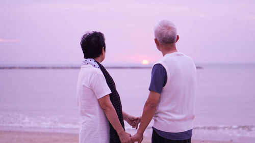 Rear view of couple standing at beach against sky