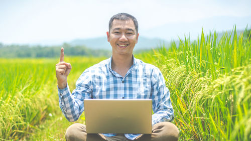 Portrait of smiling man holding laptop in field