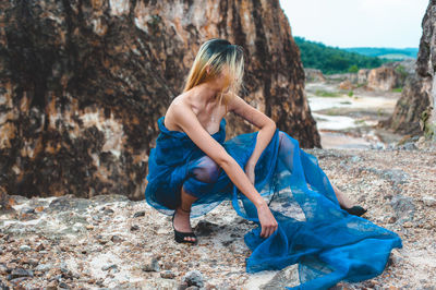 Young woman wrapped in blue fabric crouching on rock formation