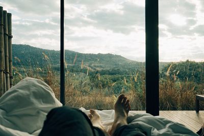 Low section of man relaxing bed against window