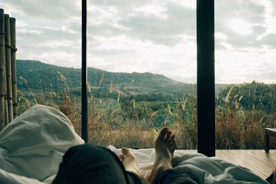 Low section of man relaxing on bed against sky