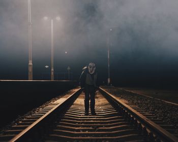 Man wearing spooky mask while standing on railroad track during halloween