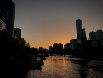 River amidst buildings in city against sky during sunset