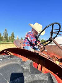 Toddler boy in cowboy hat and flannel sitting on antique tractor.