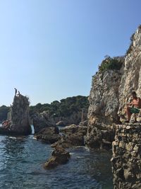 Man sitting on rocks by sea against clear sky