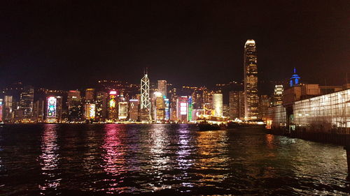 Illuminated buildings by river against sky at night