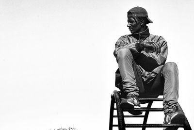 Low angle view of man sitting against clear sky