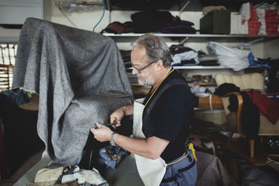 Senior male owner cutting gray fabric while standing at workshop