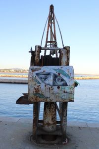 Rusty machine on pier by sea against clear sky