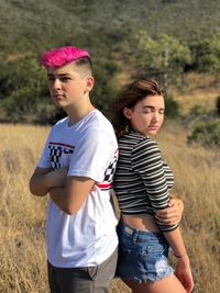 Couple back to back standing on field in sunny day