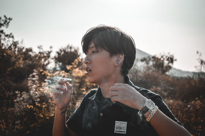 Portrait of man smoking cigarette against sky