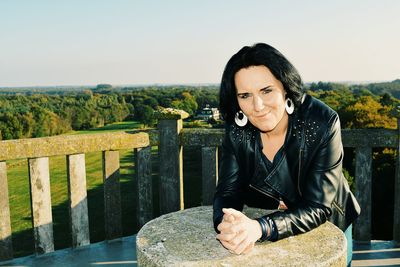 Portrait of woman leaning on stone over terrace against grassy field