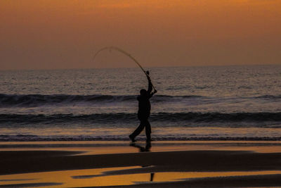 Silhouette man fishing on beach against sky during sunset