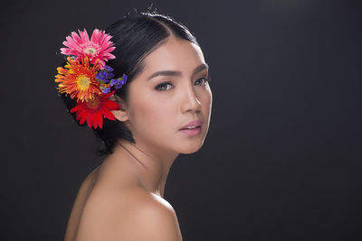 Portrait of beautiful young woman wearing flowers against black background