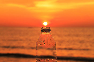 Close-up of bottle against sea during sunset