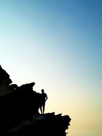 Low angle view of silhouette man standing on rock against sky