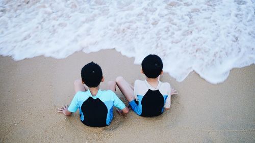 Rear view of boys sitting at shore of beach