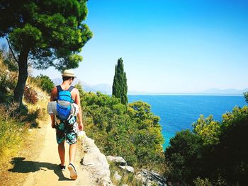 Rear view of man walking by sea against clear sky