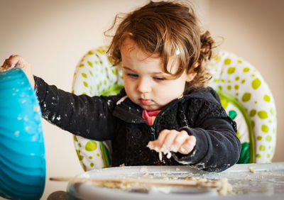 Close-up of baby girl holding dough in bowl on table at home