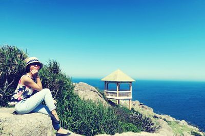 Woman sitting by sea against clear sky