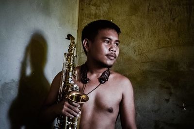 Man holding saxophones while standing against wall at home