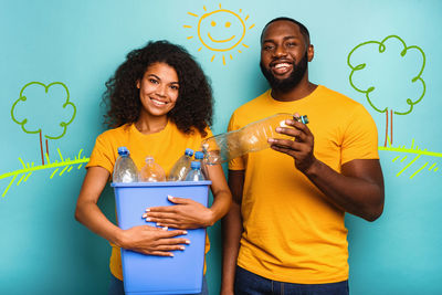 Portrait of smiling young woman drinking bottles against wall