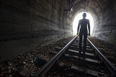 Rear view of woman standing on railroad track in tunnel