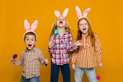 Portrait of siblings standing against yellow background