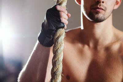 Midsection of shirtless man holding rope