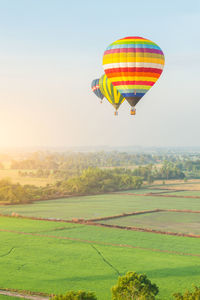 Hot air balloon flying over field against clear sky