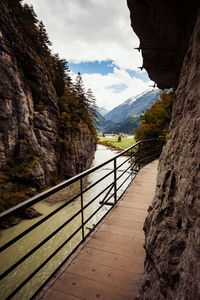 Footbridge leading towards mountains against sky