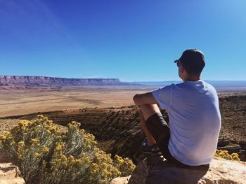 Rear view of man standing on desert against clear blue sky