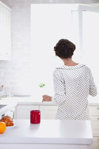 Rear view of woman standing by table at home