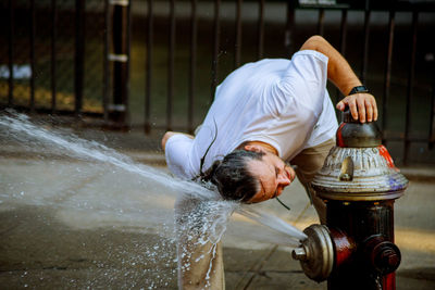 Man washing head in flowing water from fire hydrant in city