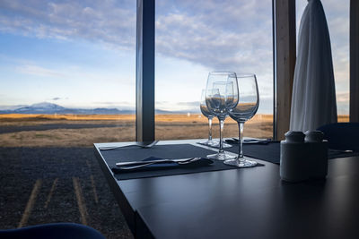 Wineglasses on table against window with view of sky at restaurant in resort