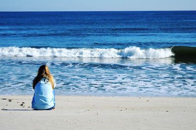 Rear view of woman sitting at sandy beach