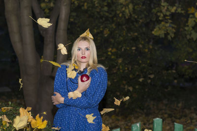 Autumn leaves falling on young woman standing at park