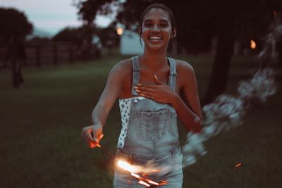 Portrait of smiling young woman burning sparkler outdoors