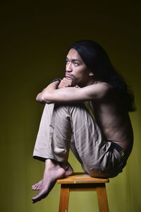 Side view of young man looking away while sitting on stool