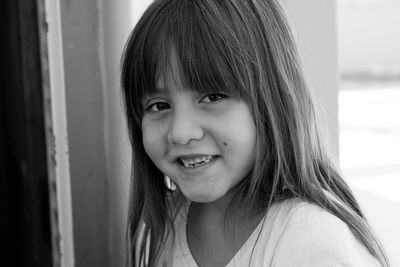 Close-up portrait of cute girl smiling while standing against wall