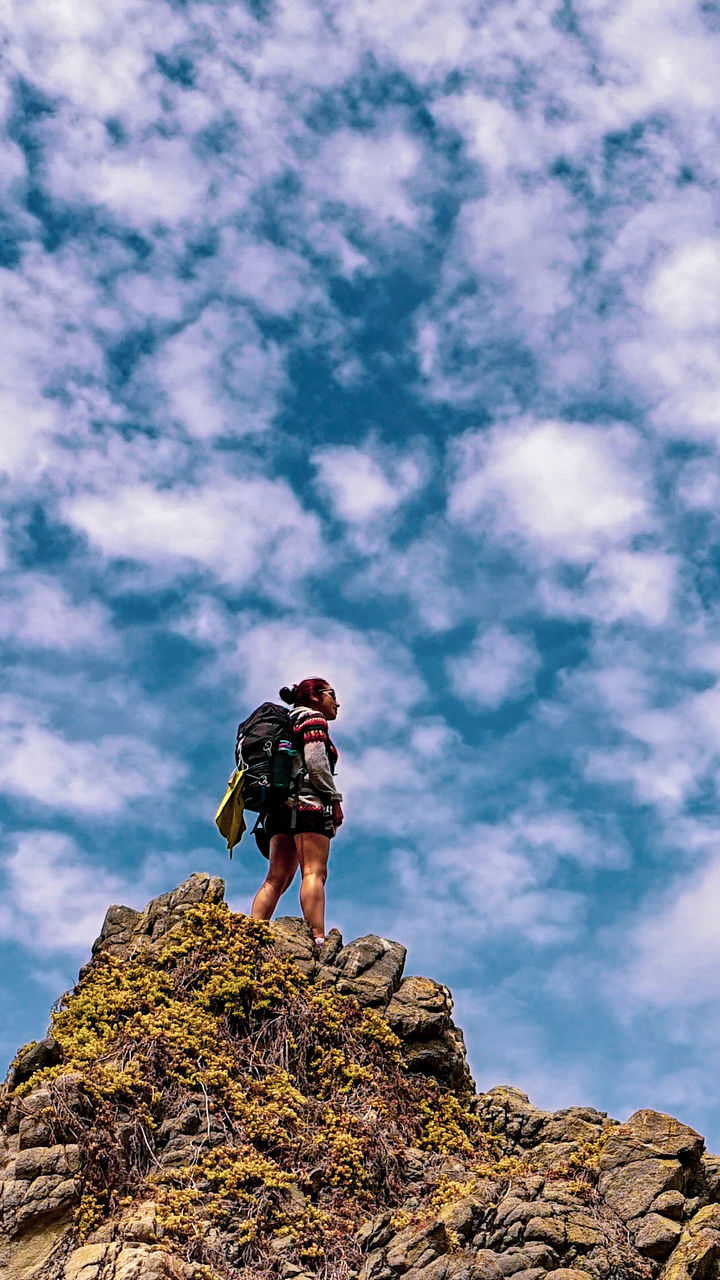full length, one person, real people, low angle view, rock, cloud - sky, sky, rock - object, solid, leisure activity, day, standing, lifestyles, nature, activity, casual clothing, beauty in nature, outdoors, adventure