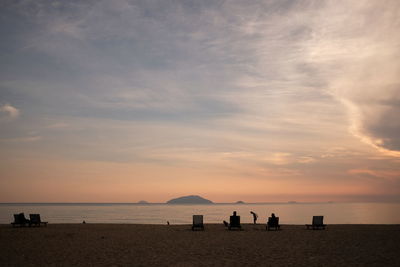 Silhouette people on beach against sky during sunset