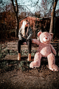 Full length of woman with teddy bear sitting on bench in park