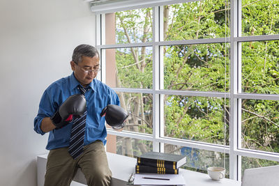 Businessman wearing boxing gloves sitting by window at office