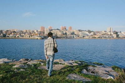 Rear view of man standing by sea against city