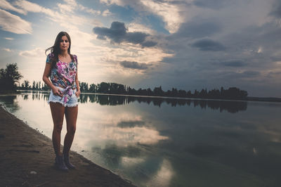 Woman standing by lake against sky during sunset