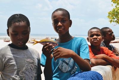 Portrait of smiling boy holding dead fish by friends at beach