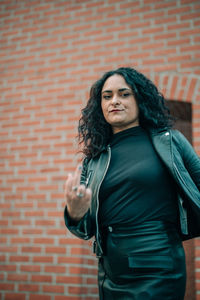 Portrait of woman showing middle finger against wall