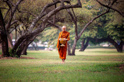 Full length of monk walking on grassy field at park